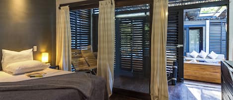 A modern bedroom with a bed, bedside lamp, and a view of an outdoor seating area through a sliding door.