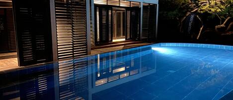 A modern house with a swimming pool, large windows, and a well-lit exterior.