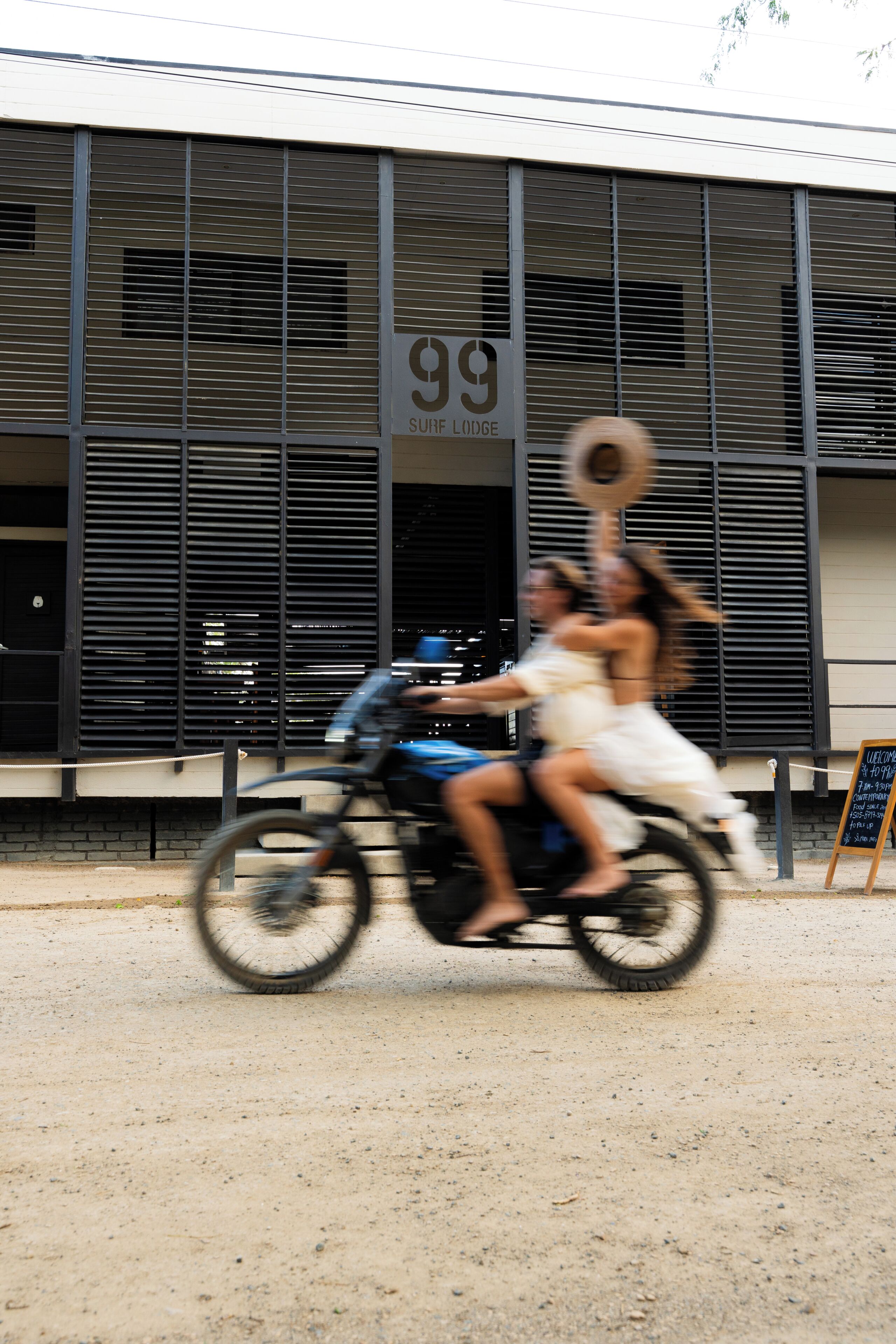 A building with a sign reading '99 Surf Lodge' and a motorcycle with two passengers.