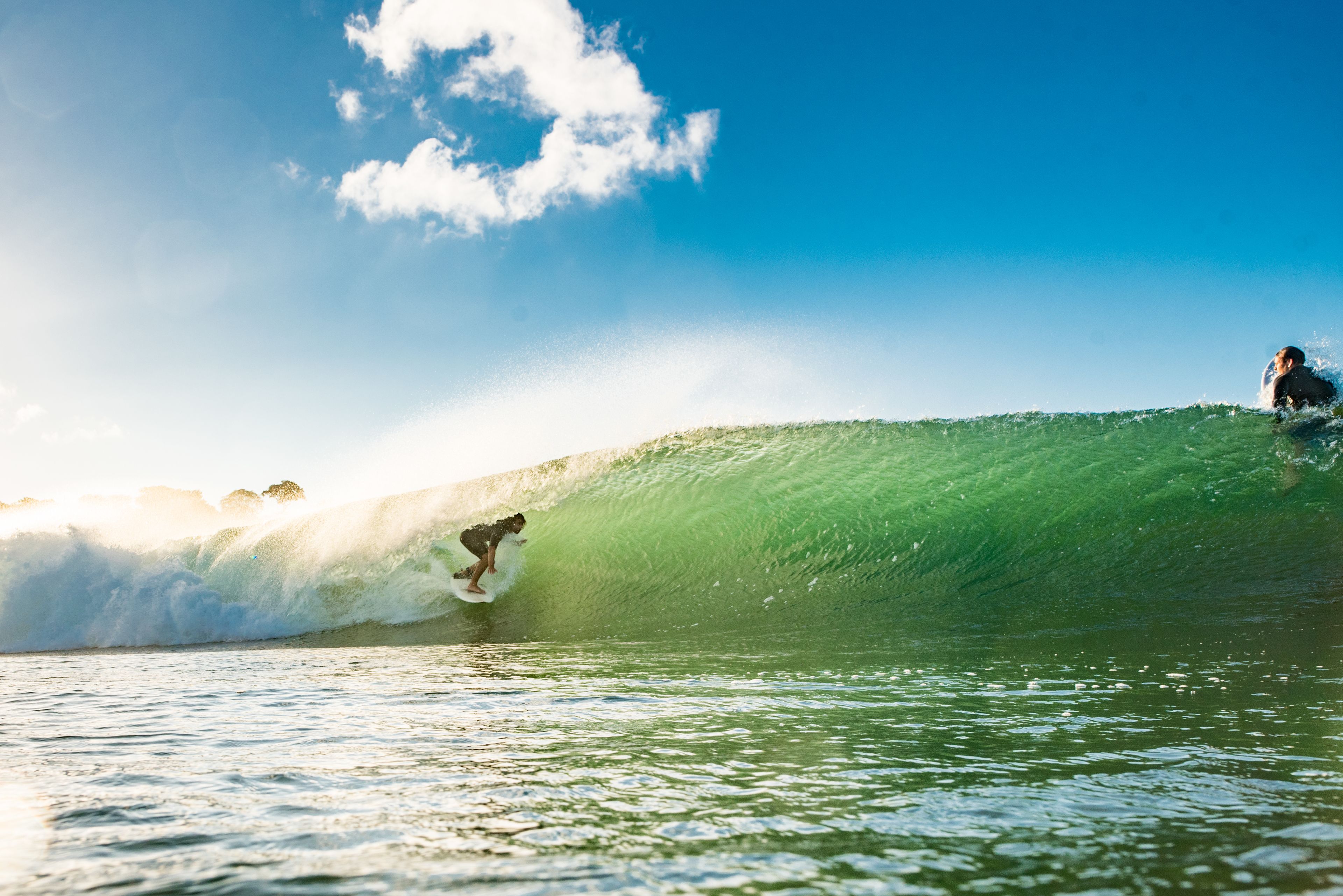 A surfer riding a large wave with clear skies in the background.