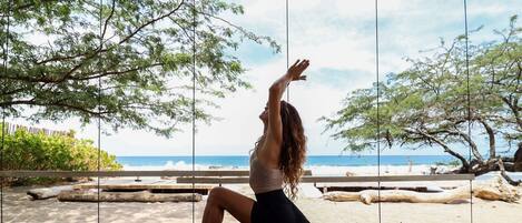 Una persona realizando una postura de yoga en una terraza de madera con vista a la playa y al océano.