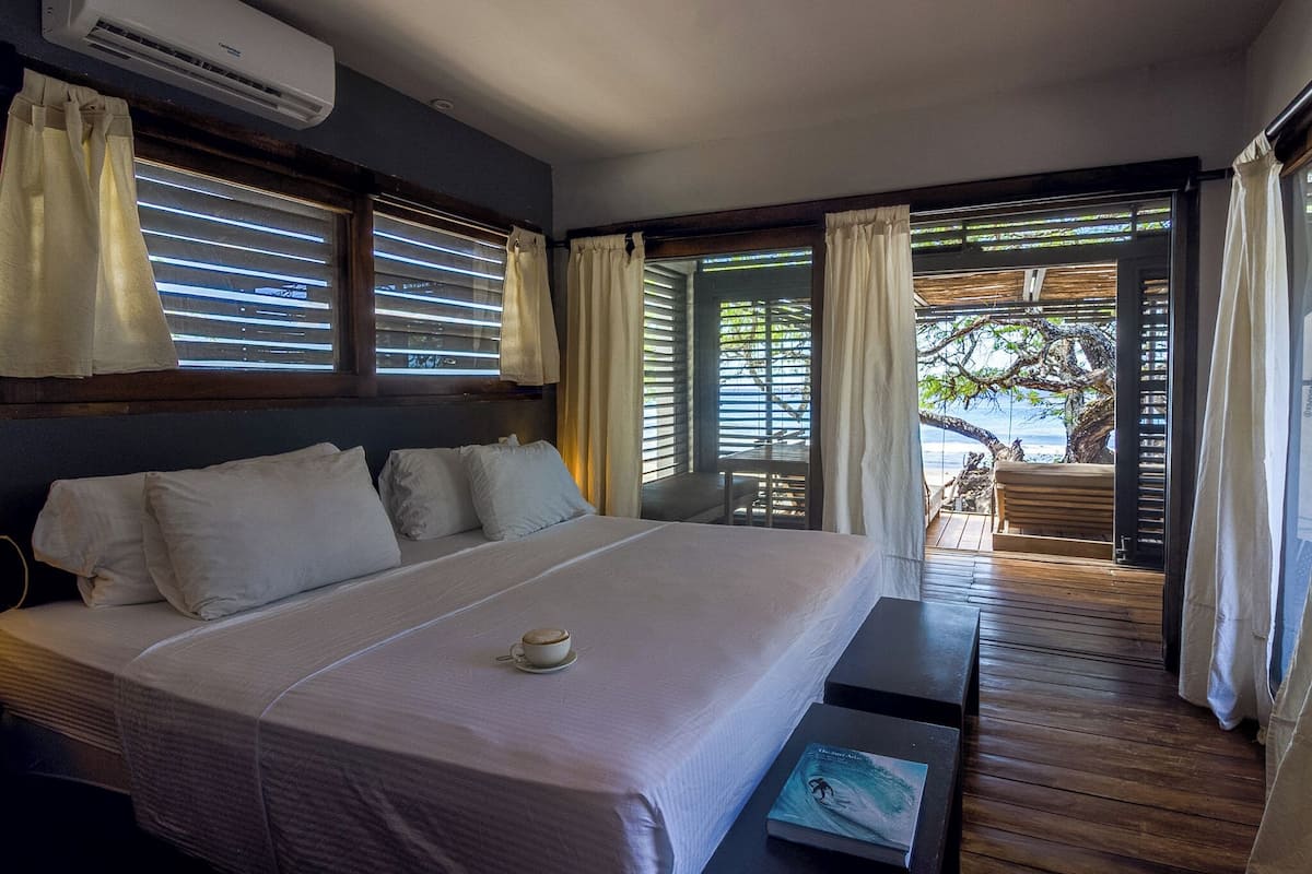 A hotel room with a bed, a coffee cup, a book, and a view of the beach through the window.