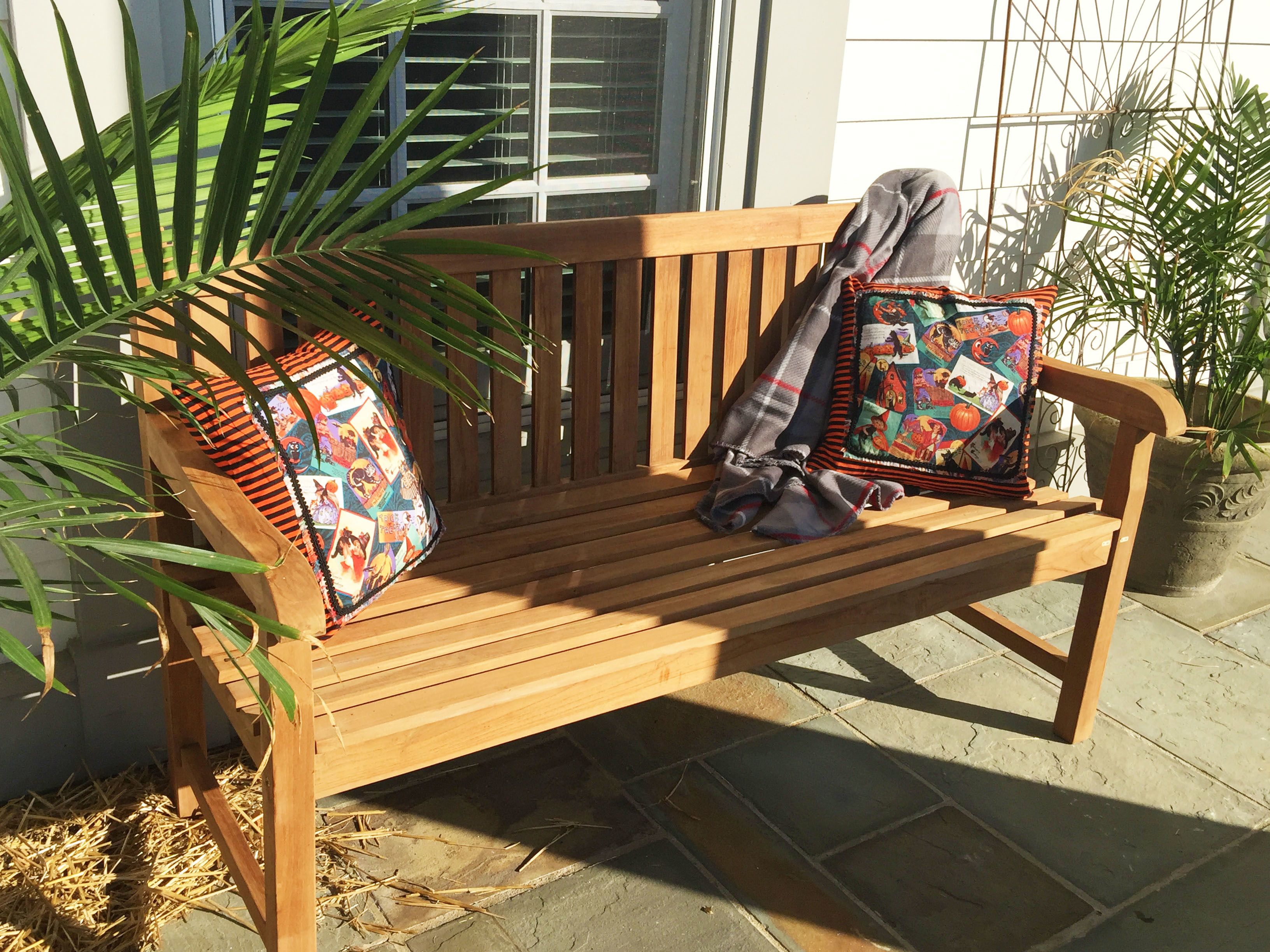 A wooden bench with two colorful pillows and a blanket.