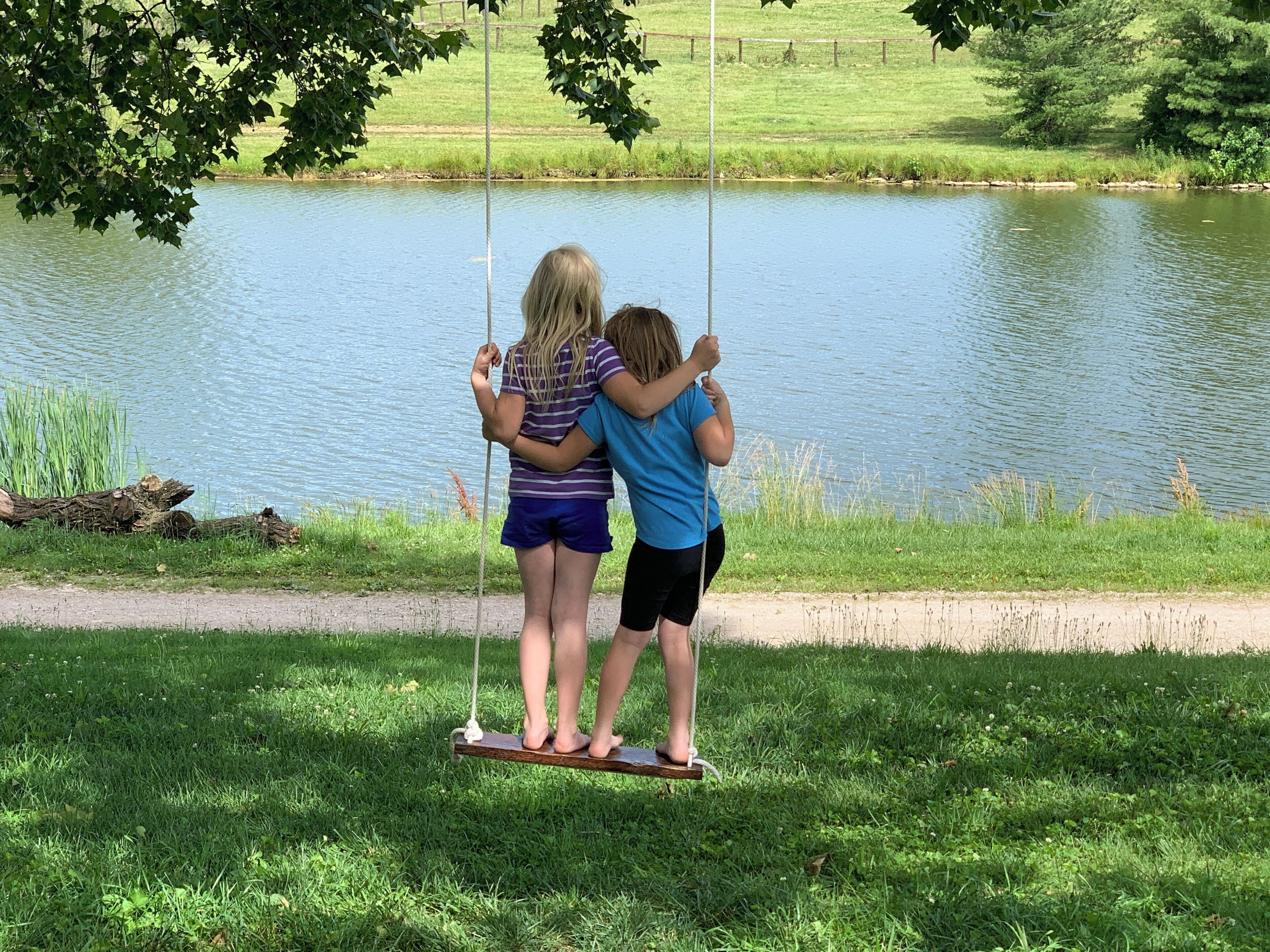 Dos niños en un columpio cerca de un lago.