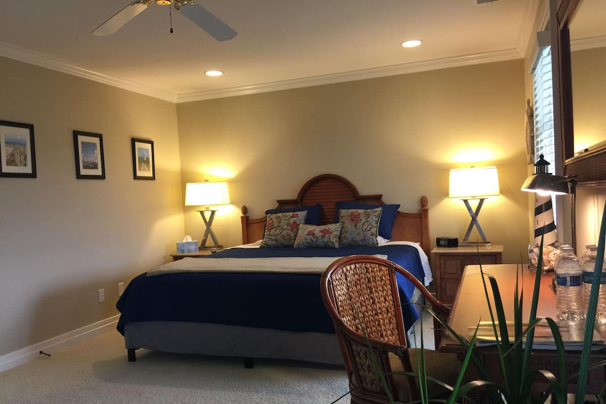 Una camera da letto con un letto, due comodini con lampade, una ventola a soffitto e una sedia.