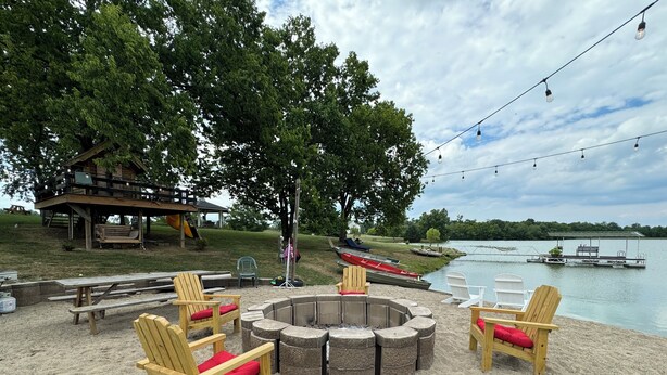 An outdoor seating area with Adirondack chairs and a fire pit, overlooking a lake with boats and a dock. - The B & B at Queenslake (Georgetown)