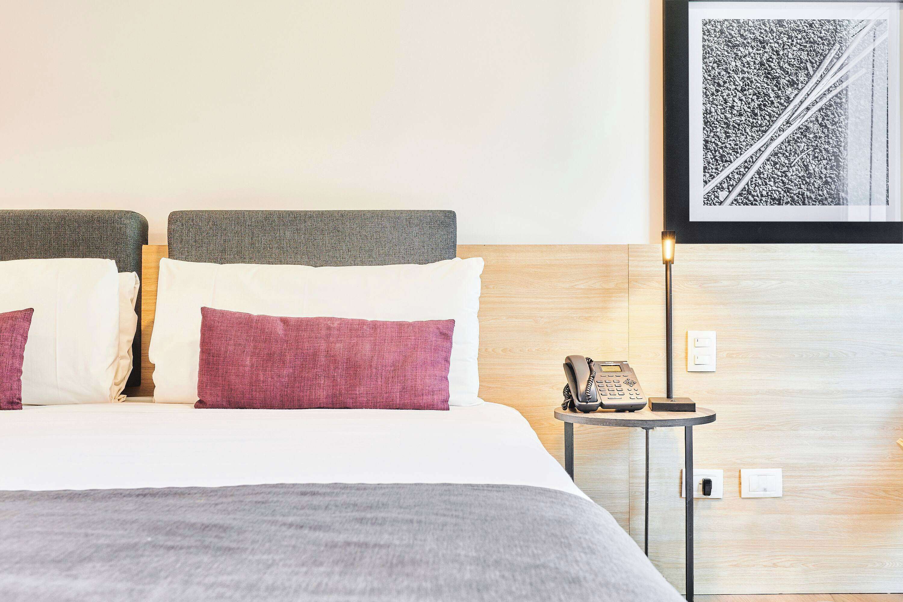 Una habitación de hotel con cama, una mesita de noche con teléfono y un cuadro en la pared.