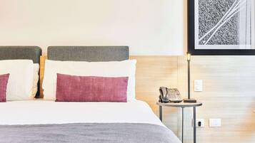Una camera d'albergo con un letto, un comodino con il telefono e un quadro appeso al muro.
