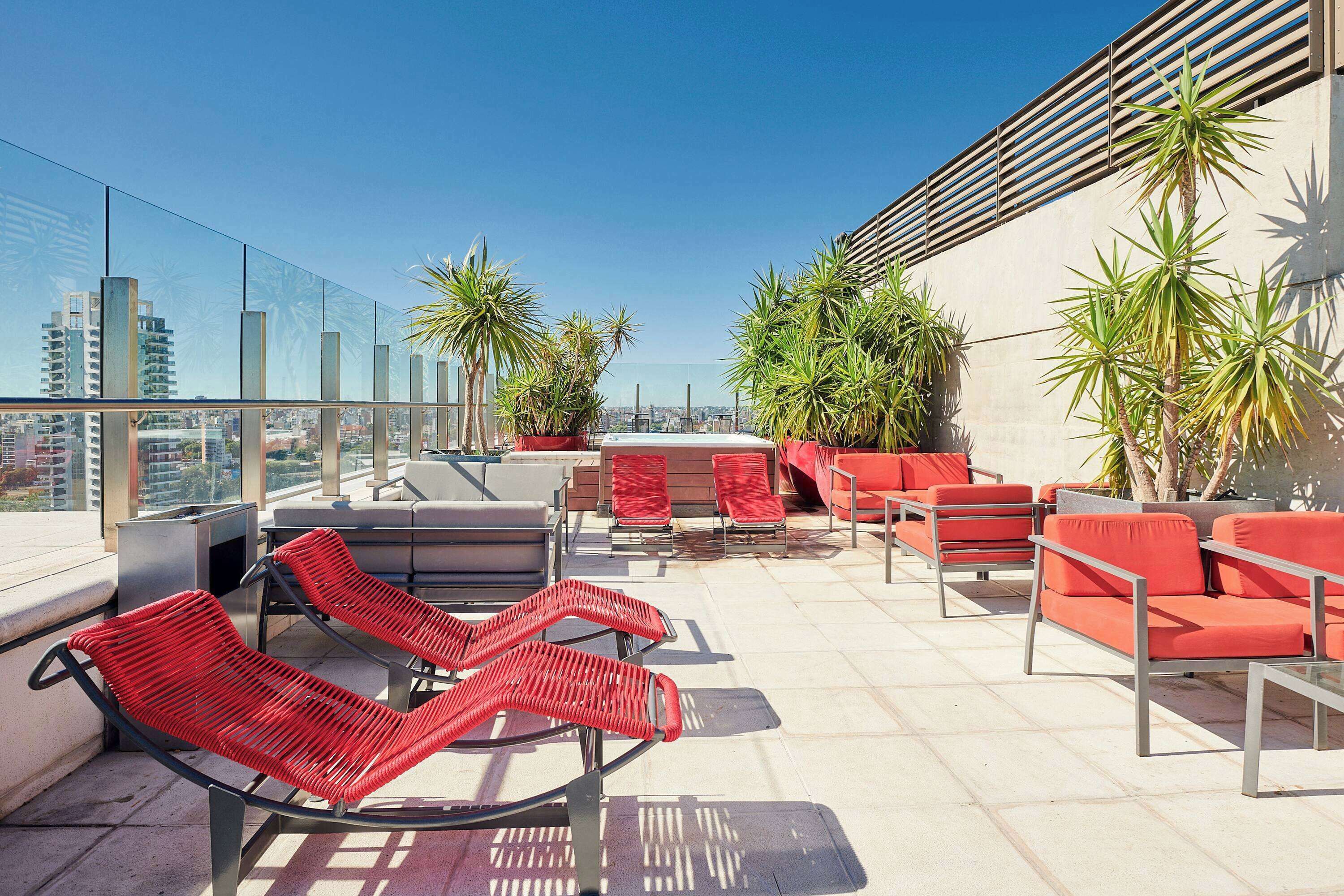 A rooftop terrace with red lounge chairs, a barbecue area, and potted plants.