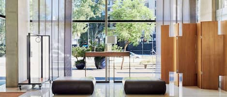 Un vestíbulo moderno con pared de vidrio, una mesa de madera y dos zonas de estar con asientos de cuero.