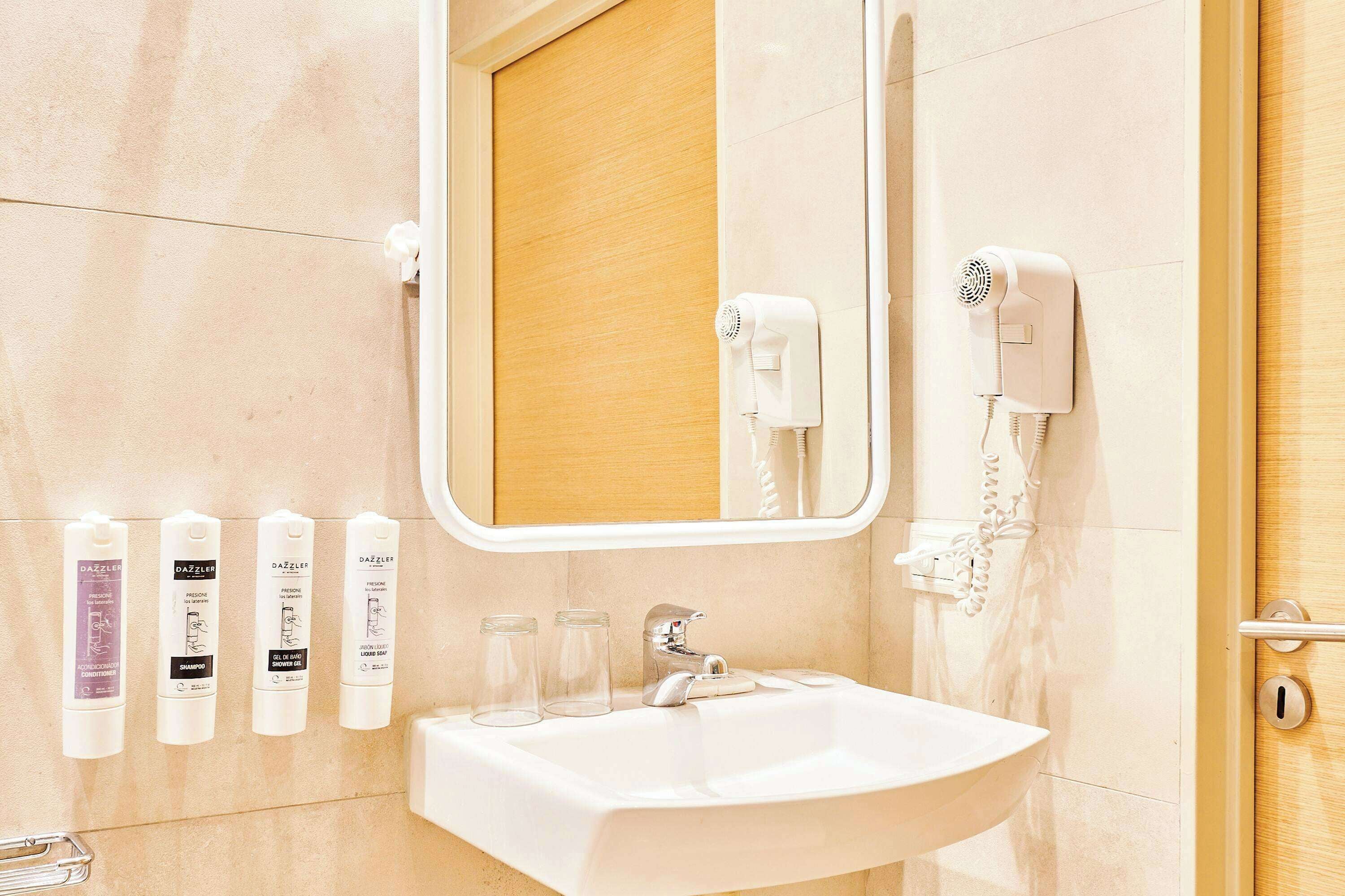 A bathroom with a white sink, a mirror, and four hairdryer bottles on the wall.