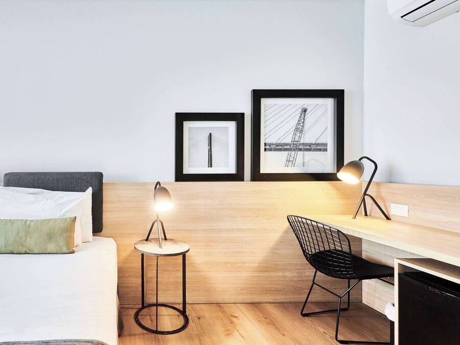 Quarto de hotel moderno com uma cama, uma escrivaninha, uma cadeira e duas molduras na parede.
