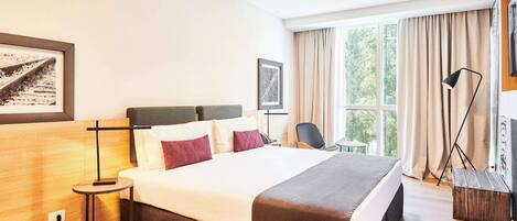Une chambre d’hôtel avec un grand lit, une table de chevet, une chaise, un bureau, une lampe et une fenêtre avec des rideaux.
