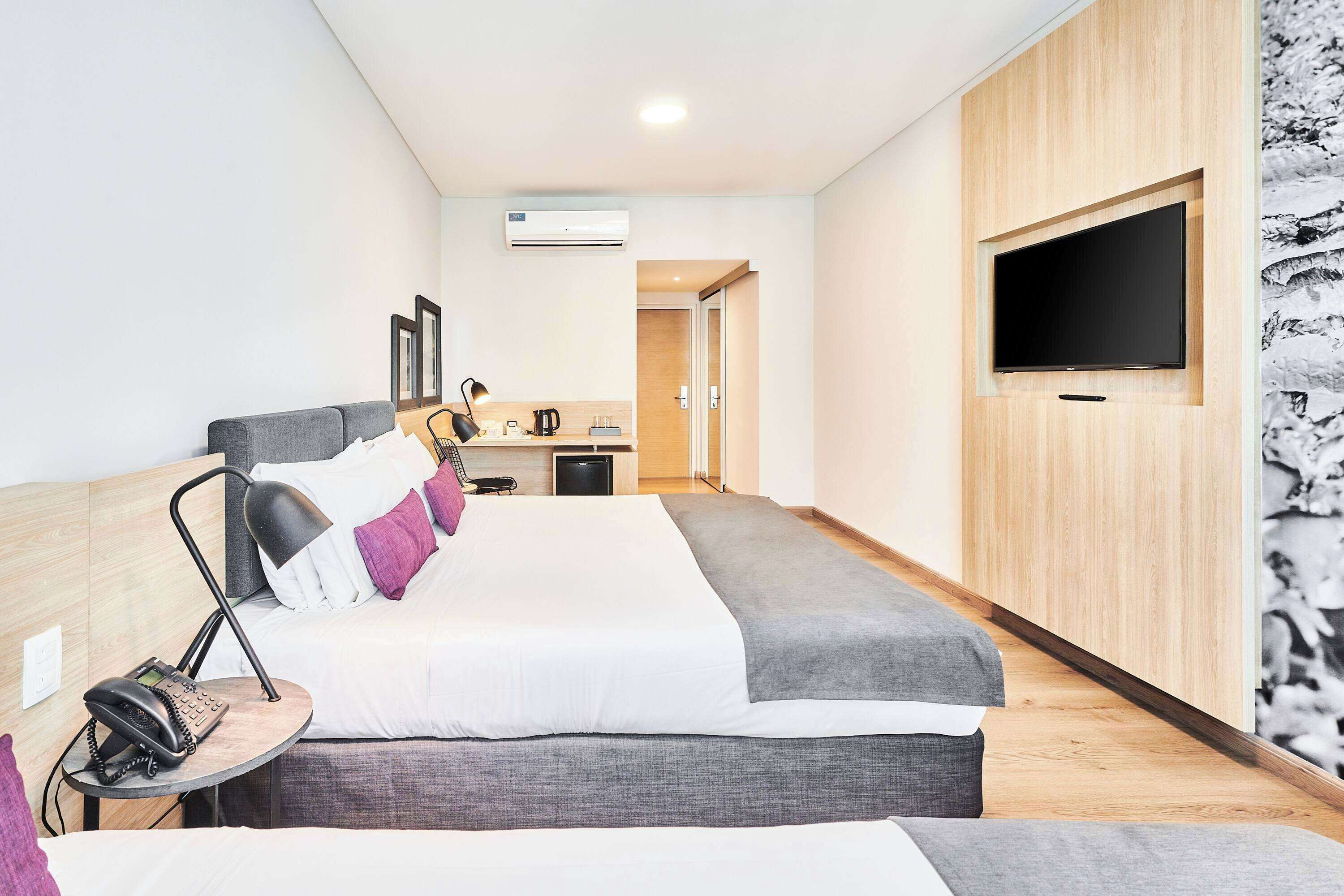 Une chambre d’hôtel avec deux lits, un bureau avec une lampe, un téléphone et un téléviseur fixé au mur.