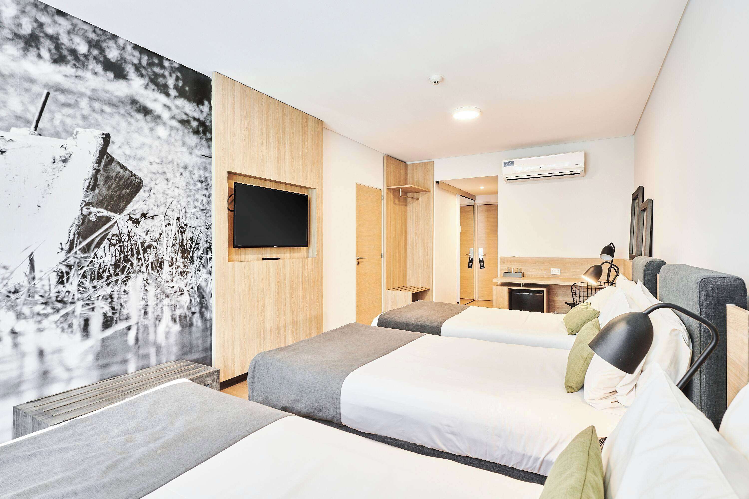 A hotel room with three beds, a TV, a desk, and a bathroom.