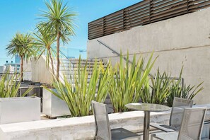 A rooftop terrace with a concrete wall, metal chairs, a round table, and tall green plants. - Dazzler by Wyndham Rosario (Rosario)