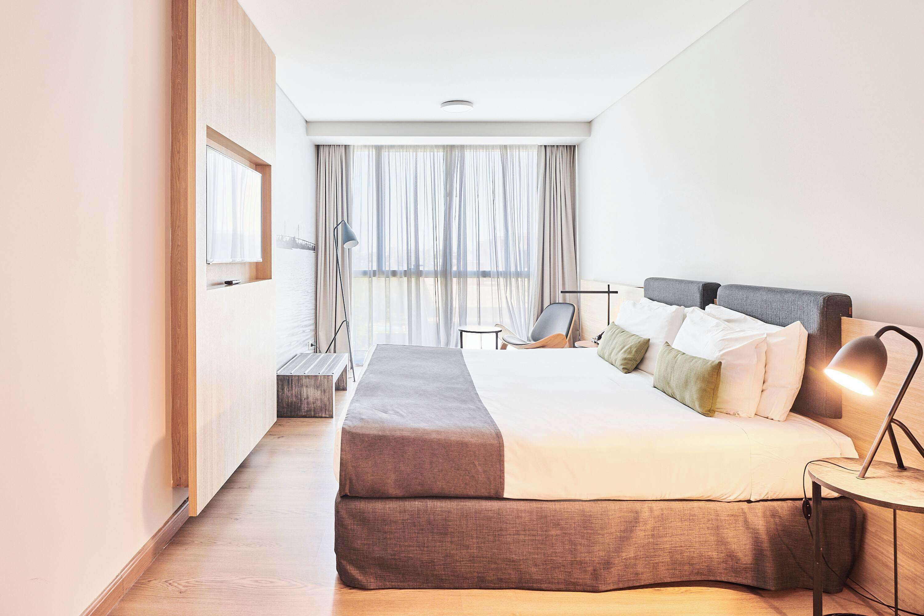 A modern hotel room with a large bed, a desk, and a chair.