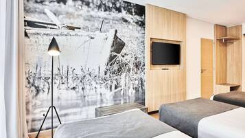 Habitación de hotel con dos camas, un televisor de pared grande y un mural de un barco en el agua.
