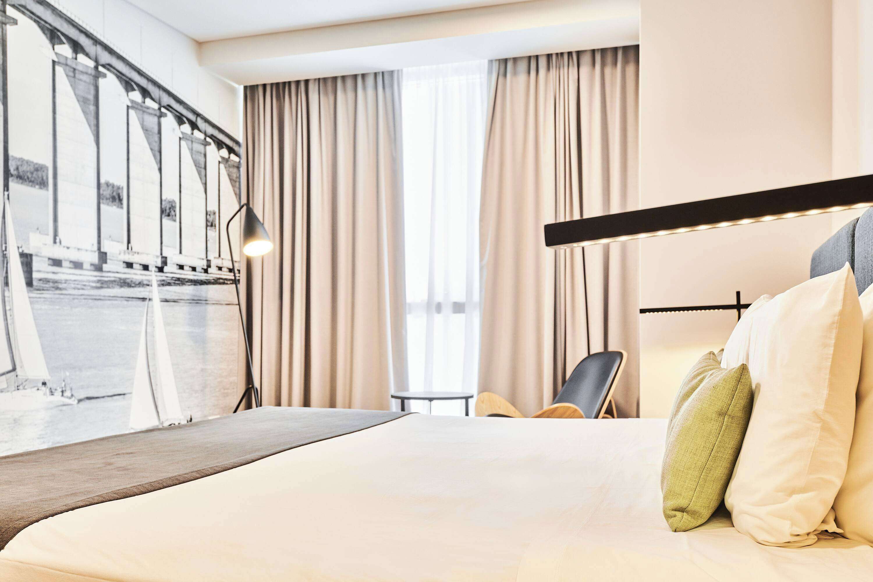 A hotel room with a large bed, a view of a bridge, and a modern lamp.