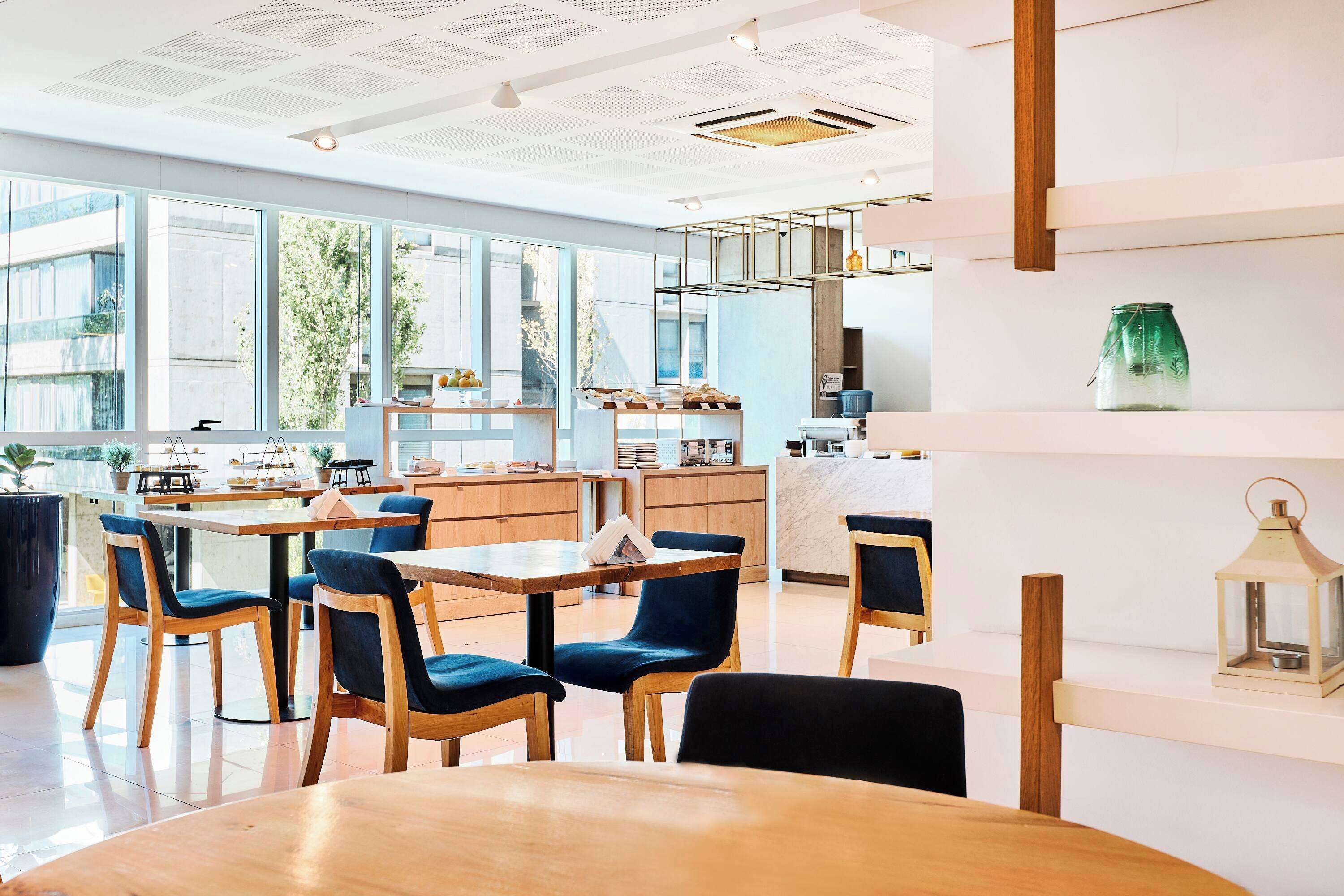 A modern cafe with wooden tables and chairs, large windows, and a clean, bright interior.