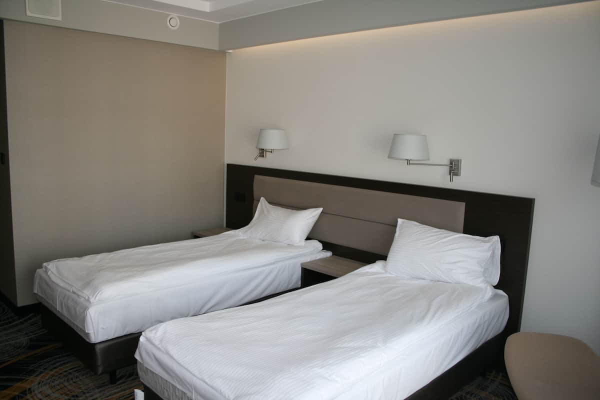 A hotel room with two single beds, a headboard, and two wall-mounted lamps.