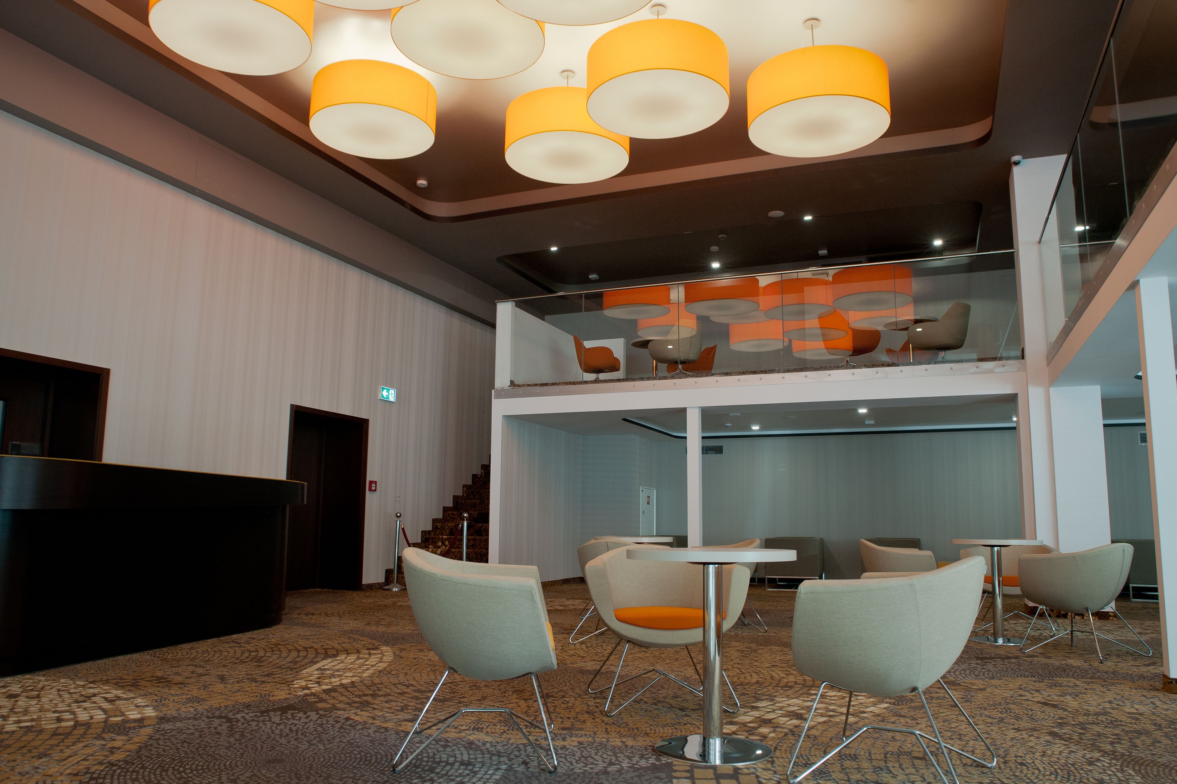 A modern hotel lobby with a reception desk, seating area, and a glass railing overlooking a lower level.