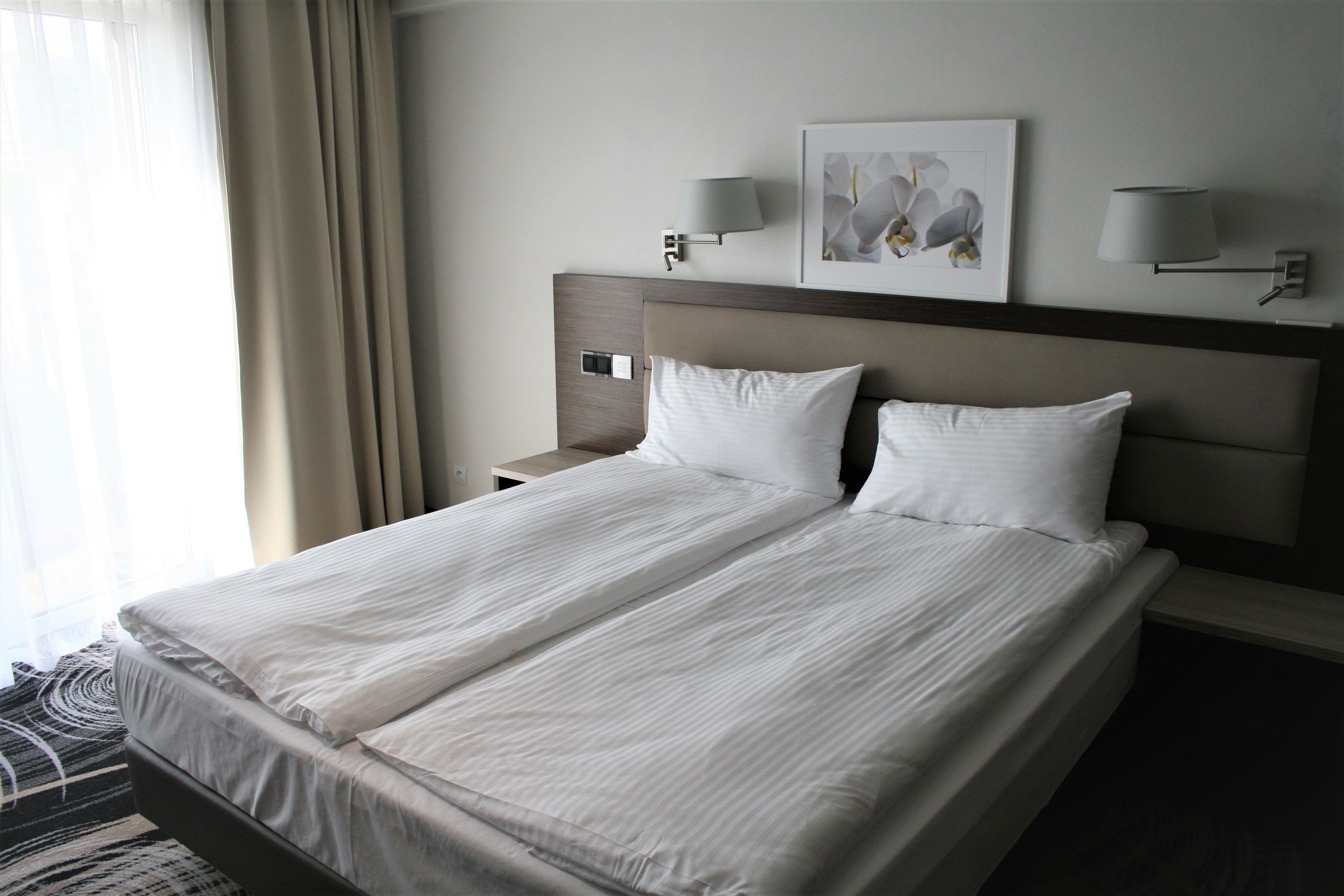 Ein Hotelzimmer mit einem großen Bett, zwei Nachttischlampen, einem Nachttisch und einem gerahmten Bild an der Wand.
