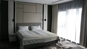A modern hotel room with a large bed, built-in storage, a flat-screen TV, and a large window with curtains.