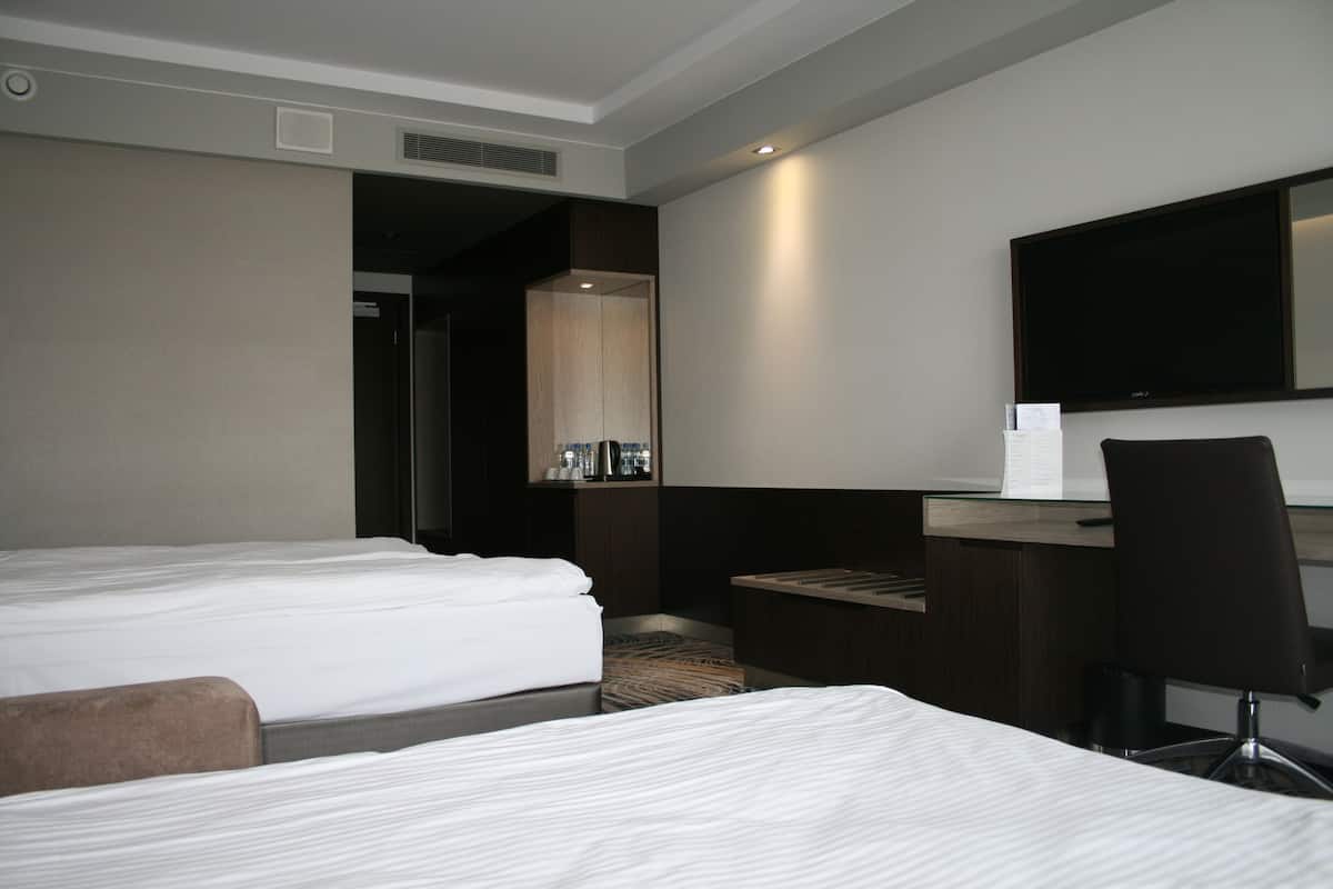 A hotel room with two beds, a desk, a chair, a flat-screen TV, and a mirror.