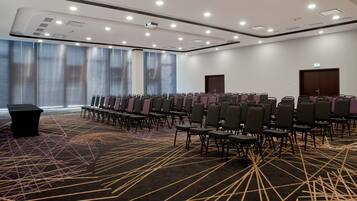 Une salle de conférence avec des rangées de chaises, une table noire et un tapis à motifs.