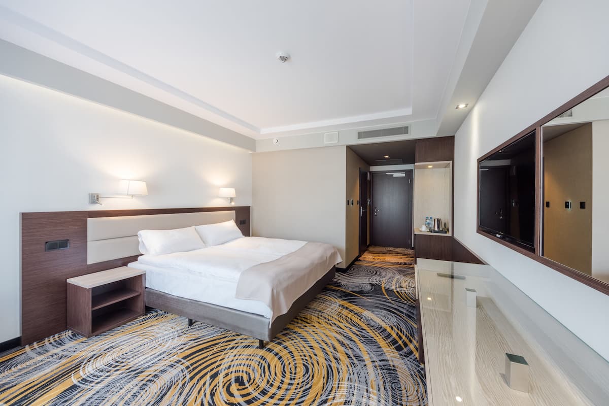 A hotel room with a large bed, bedside tables, a TV, and a mirror.