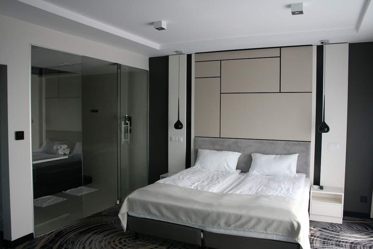 A modern hotel room with a large bed, a glass shower enclosure, and a minimalist design.