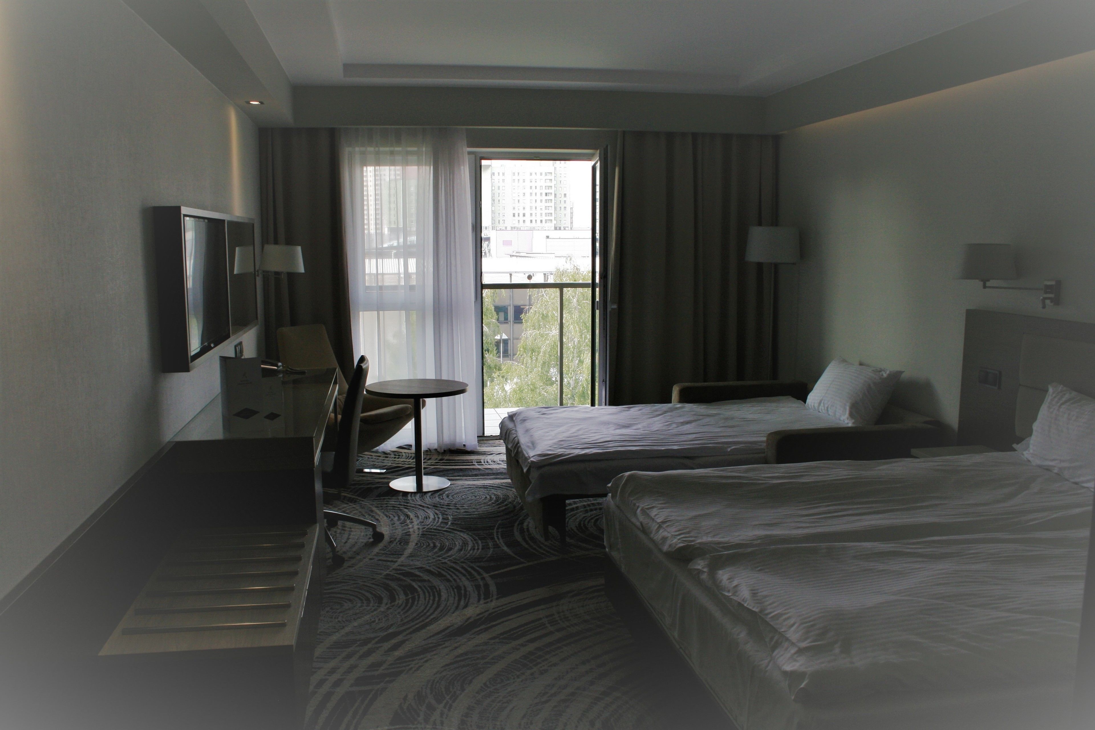 A hotel room with two beds, a desk, a chair, a TV, and a window with curtains.