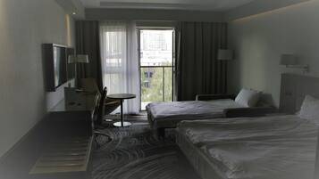 A hotel room with two beds, a desk, a chair, a TV, and a window with curtains.