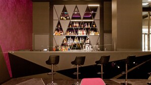 Zona de bar con diseño moderno, destacando una exhibición central de botellas y una barra.