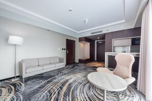 A modern hotel room with a sofa, a round table, a kitchenette, and a patterned carpet. - Hotel Ambasador Premium (Lodz)