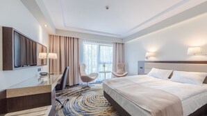 Una habitación de hotel con cama, escritorio, silla, televisión y ventana con cortinas.