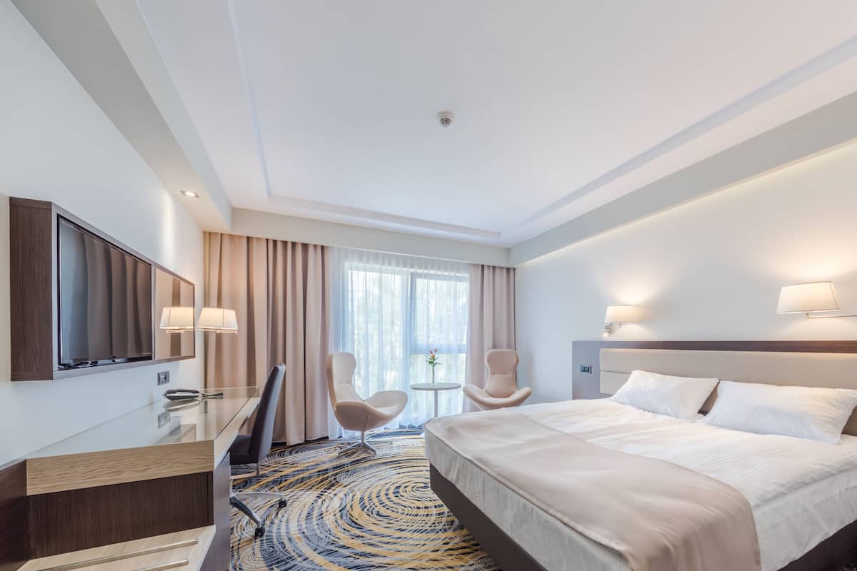 A hotel room with a bed, a desk, a chair, a TV, and a window with curtains.