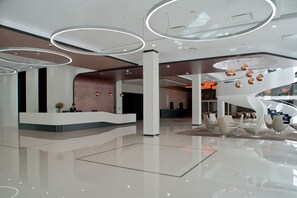 A modern lobby with a central reception desk, a spiral staircase, and contemporary lighting fixtures. - Hotel Ambasador Premium (Lodz)