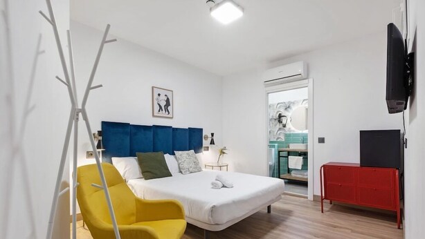A modern hotel room with a large bed, a yellow chair, a red cabinet, and a TV. - Hostel Malaga City (Malaga)