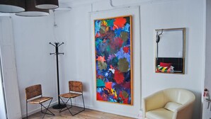 A room with a large abstract painting, two wooden chairs, a cream-colored armchair, and a floor lamp. - Hostel Malaga City (Malaga)