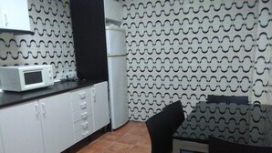 A kitchen with white cabinets, a microwave, a refrigerator, and a patterned wall. - Hostel Malaga City (Malaga)