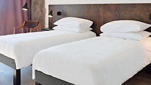 A hotel room with two beds, a nightstand with a lamp, a chair, and a neon sign on the wall.