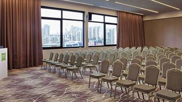 A conference room with rows of chairs, large windows with a city view, and a carpeted floor.