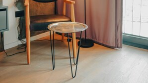 A room with a wooden chair, a small round table, a floor lamp, a curtain, and a window.