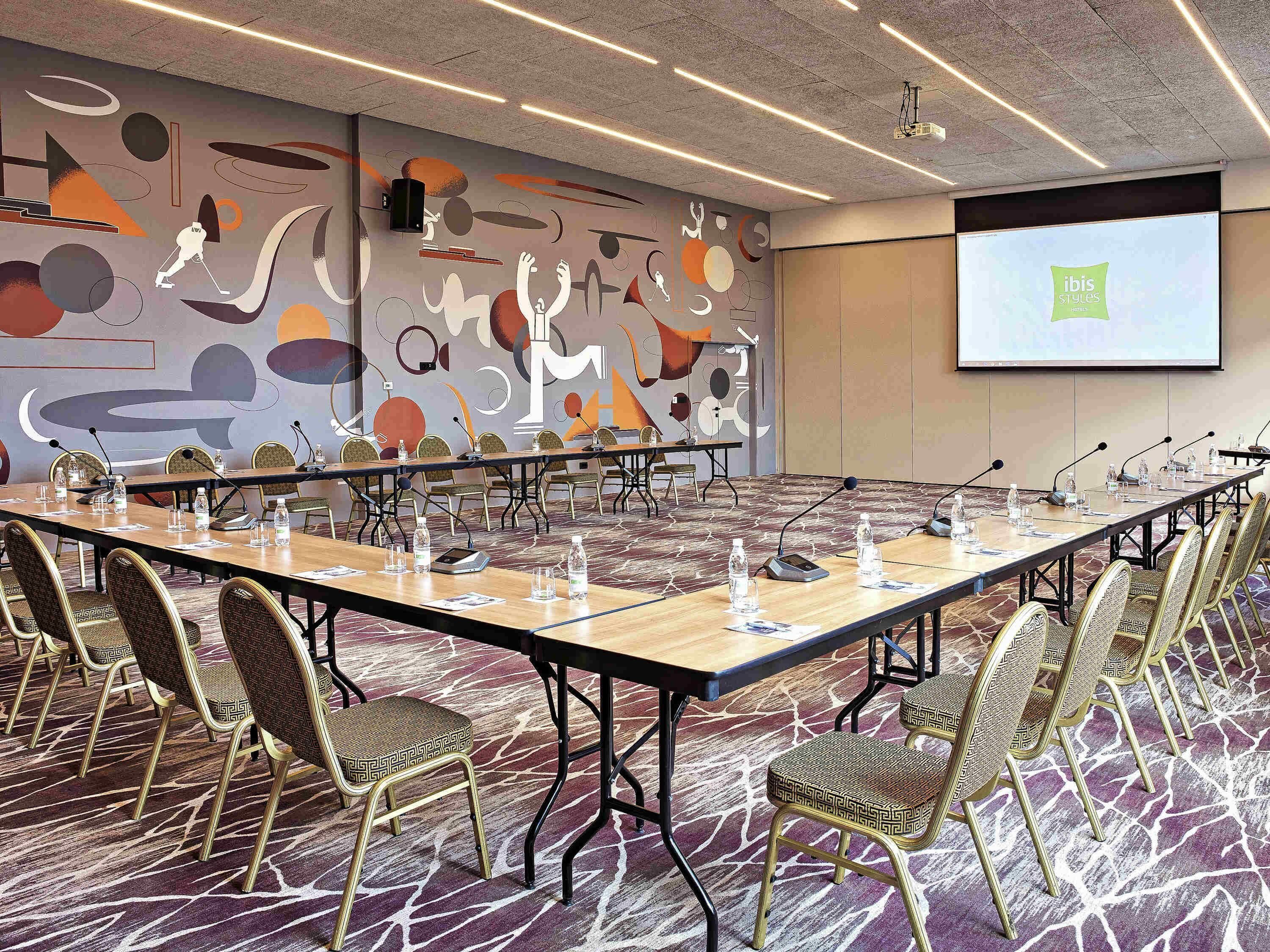 A conference room with a long table, chairs, and a projector screen displaying 'ibis Styles'.