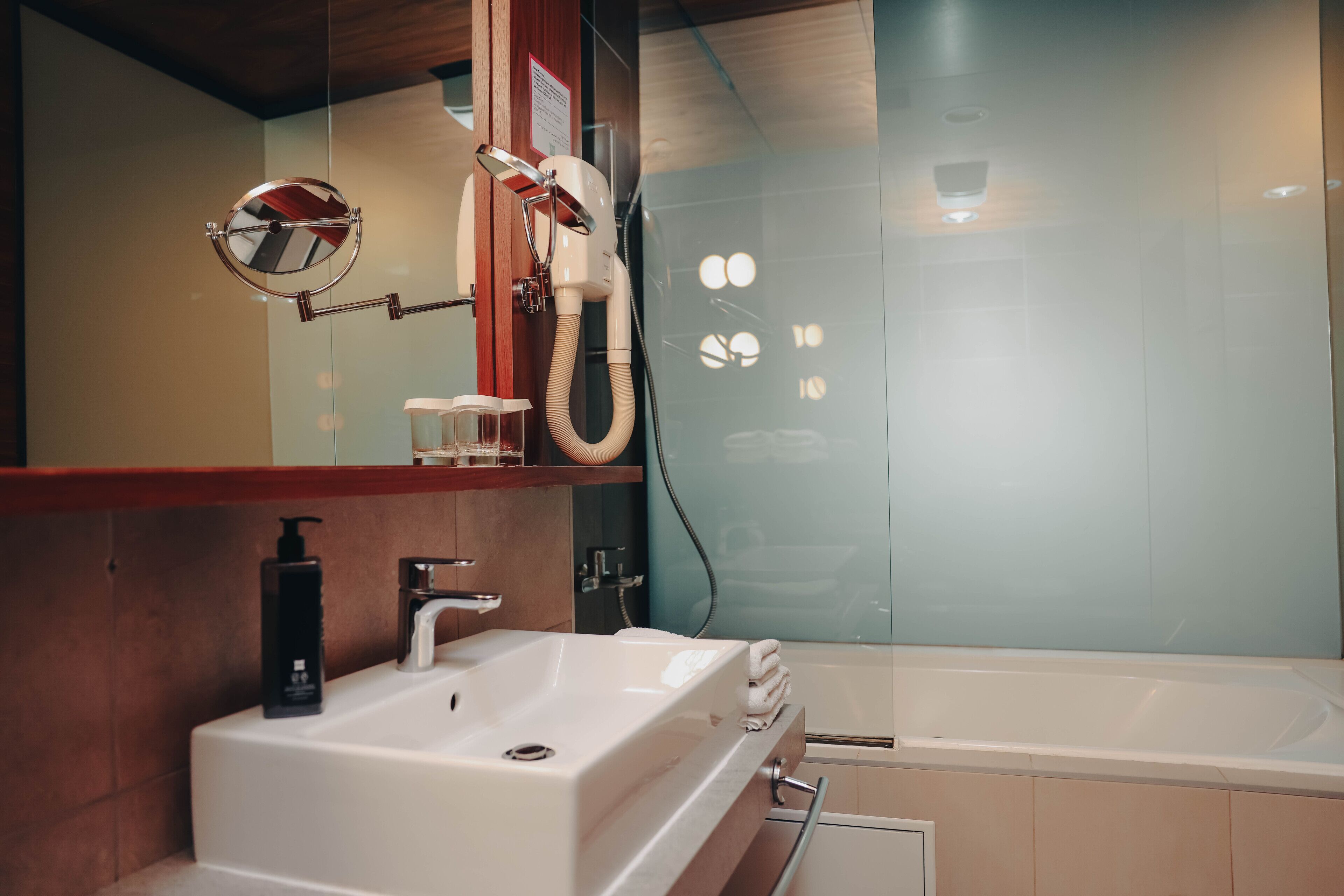 A modern bathroom with a white sink, a mirror, a handheld showerhead, and a bathtub.
