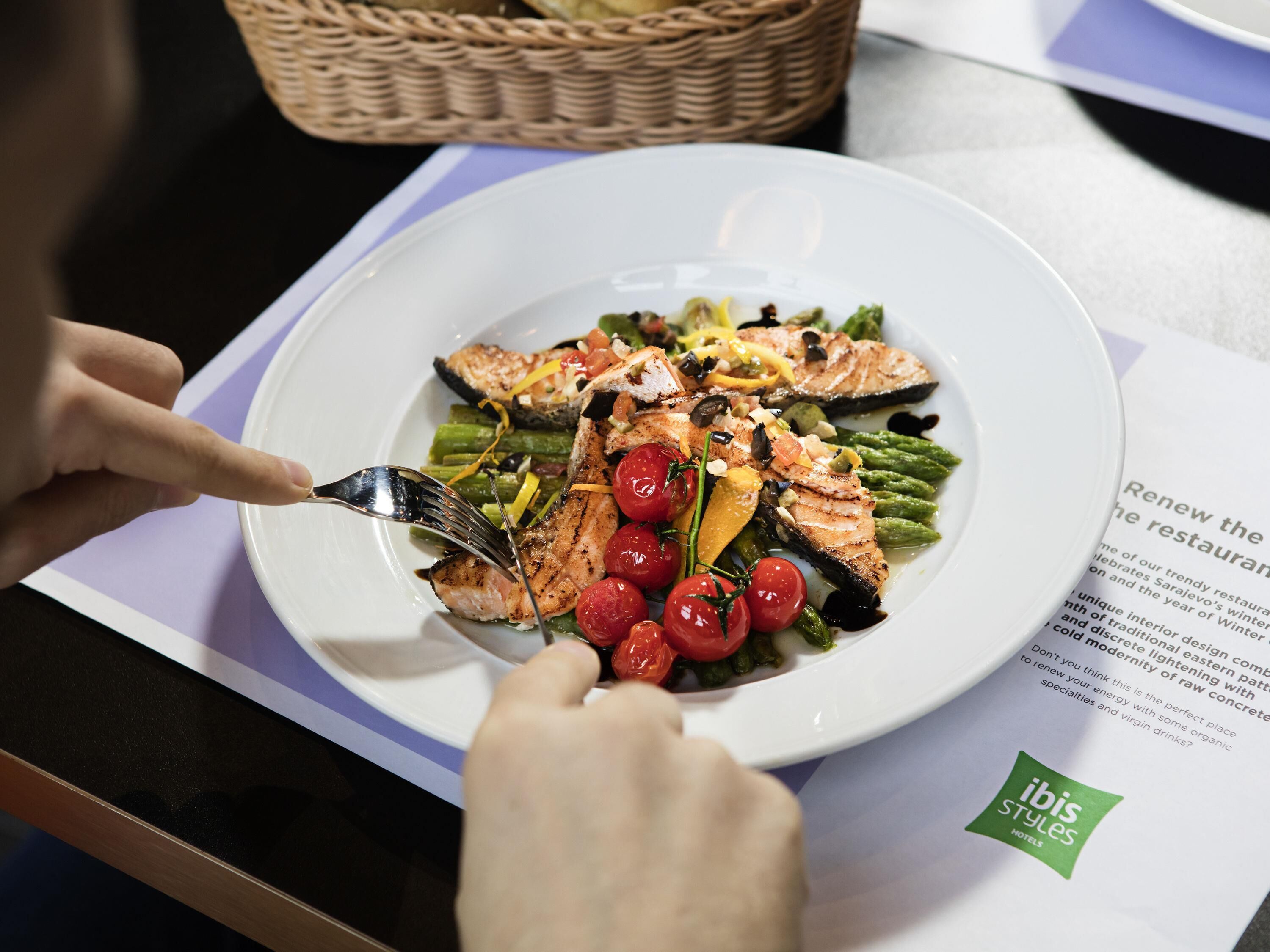 Une assiette de nourriture, une fourchette, un menu et un logo sont posés sur une table.
