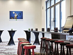 Un salón de conferencias con una larga mesa, varios taburetes, un cuadro en la pared y un amplio ventanal.