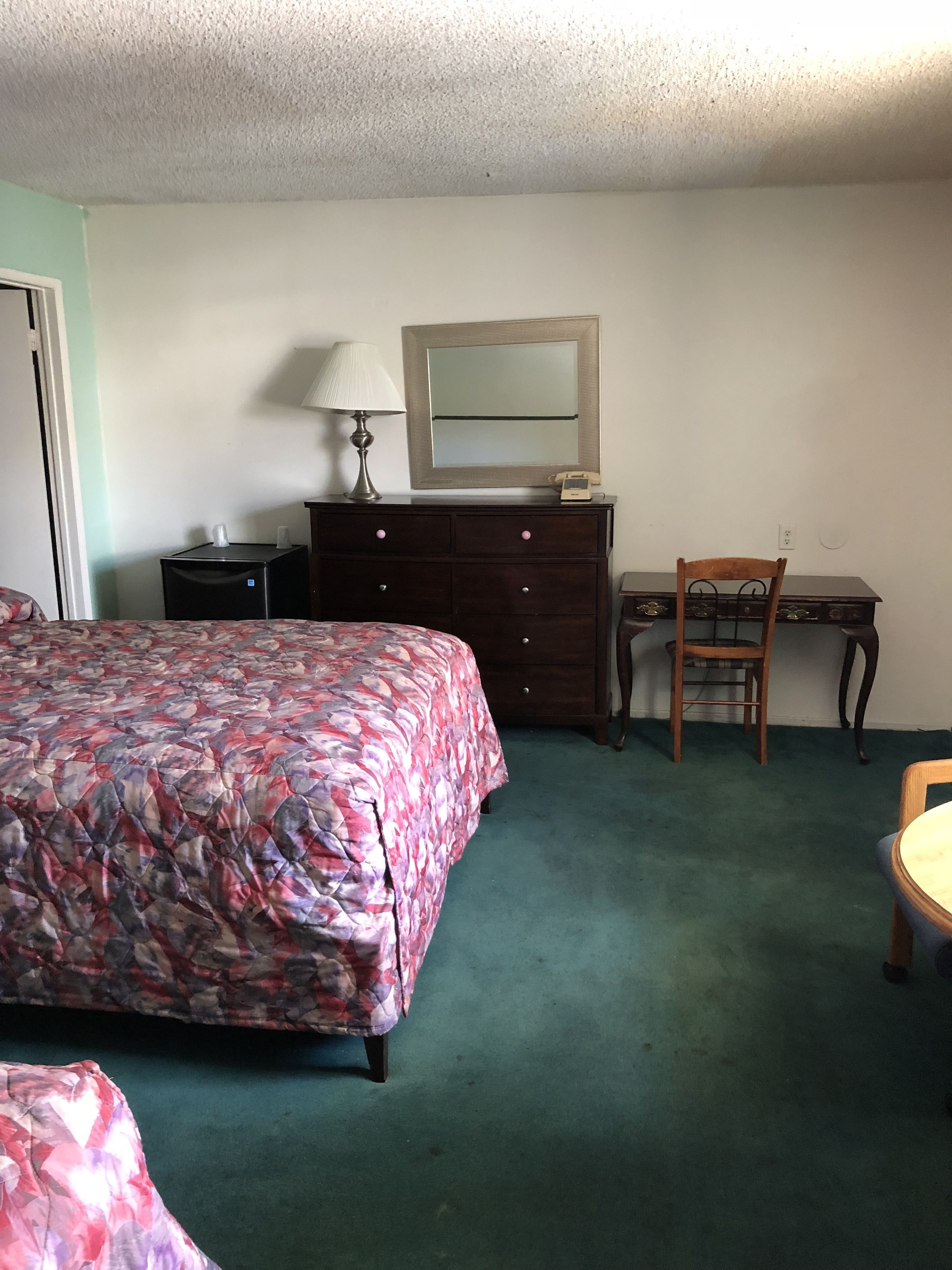 A hotel room with a bed, a desk, a chair, a dresser, and a lamp.